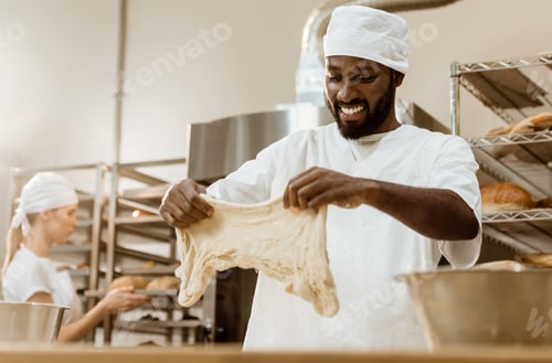 Preview: happy handsome african american baker preparing dough on baking manufacture