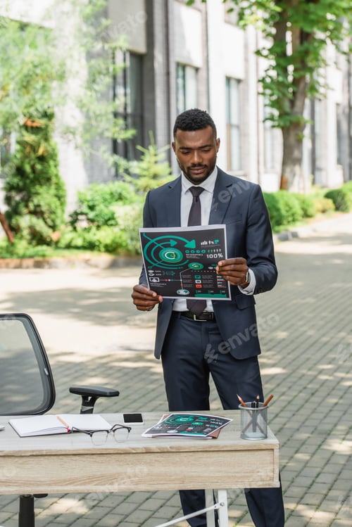 Preview: african american businessman holding printed infographics near desk outside