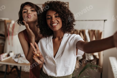 Visualização: Lindas moças em blusas modernas posam de bom humor no escritório do estilista. De pele escura