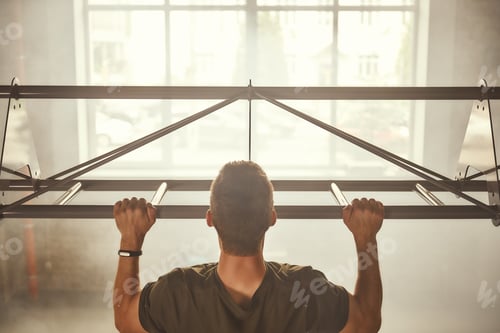 Preview: Just do it Back view of strong man doing pull-ups while exercising in the gym