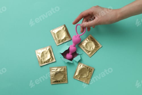 Preview: Pink anal balls with condoms on a background of torn turquoise paper