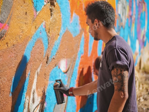 Visualização: Belo garoto talentoso fazendo um grafite colorido com spray de aerossol na parede da rua urbana