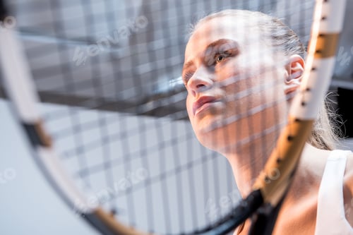 Preview: Attractive young woman holding tennis racquet and looking away