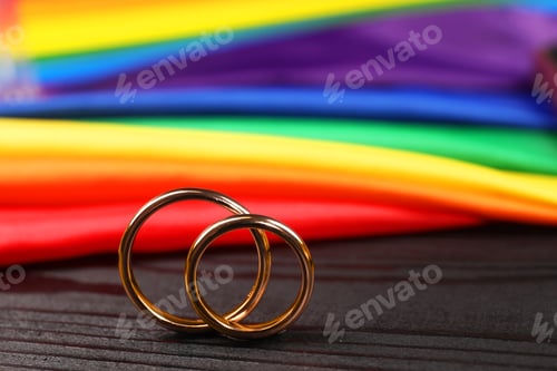 Preview: Rainbow LGBT flag and wedding rings on black wooden background, closeup