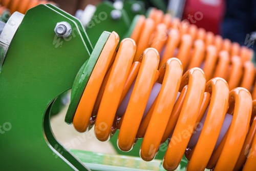 Preview: Orange hard spring made of steel. Part of big industrial or agricultural machine