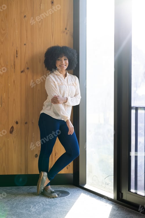 Preview: Smiling woman standing by window, wearing business casual attire in office
