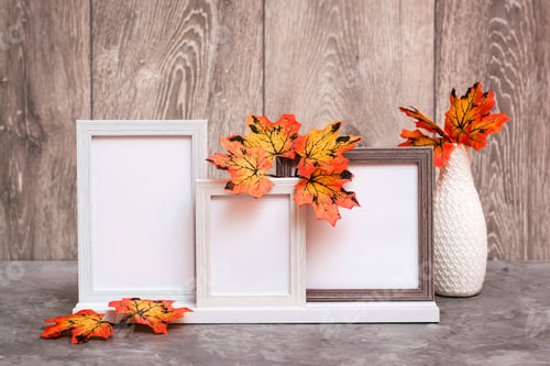 Preview: Three empty photo frames on a stand and a vase with orange maple leaves stand on the table.