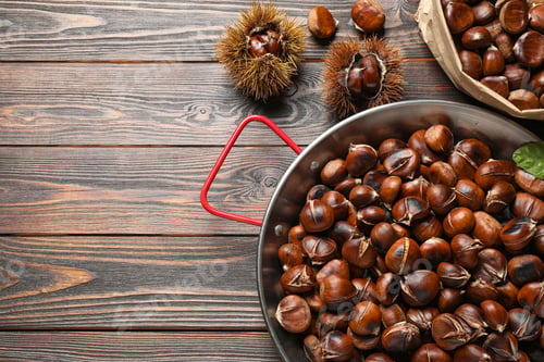 Preview: Delicious roasted edible chestnuts on brown wooden table, flat lay. Space for text