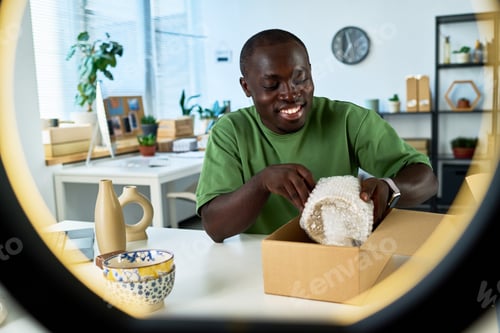 Preview: Happy young African American man putting wrapped vase into cardboard box