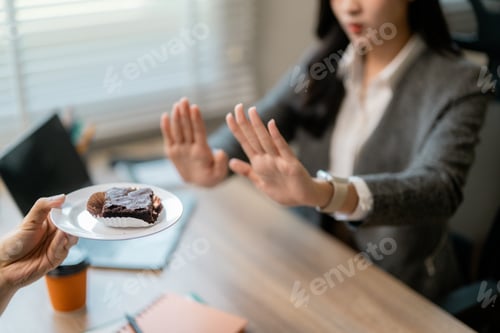 Preview: Businesswoman refusing a brownie with her hands, following a healthy diet in the office
