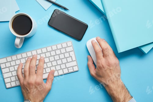 Preview: Cropped view of man using computer keyboard and computer mouse at workplace with papers, smartphone