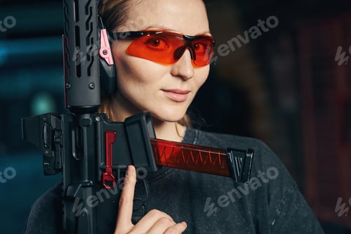 Preview: Beautiful lady in protective eyewear holding a weapon with one hand