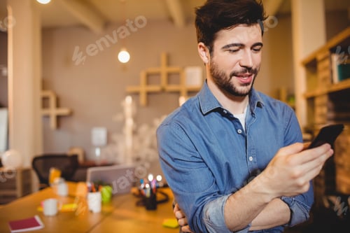 Preview: Smartphone resting on desk in open-plan office, surrounded by laptop, coffee mug and sticky notes
