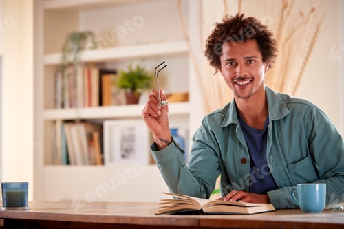 Preview: Portrait Of Man Relaxing At Home Sitting At Table Reading Book With Hot Drink