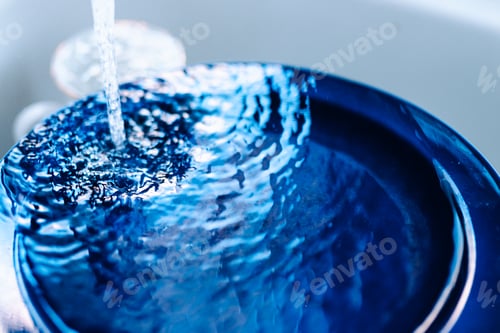 Preview: flow of water from water faucet with splashes on surface of blue plate