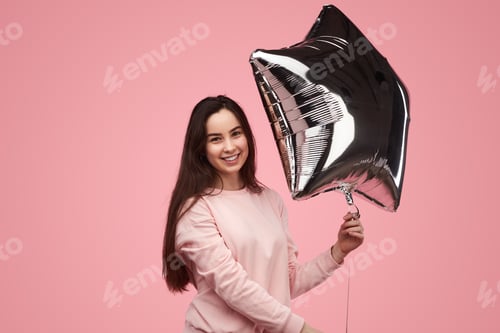 Preview: Content female millennial holding star shaped balloon in pink studio