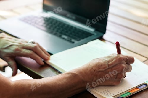 Preview: Unrecognizable old woman using a laptop and a notebook at home