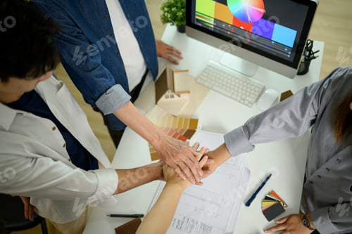 Preview: High angle view of architects or interior designers stacking hands over table