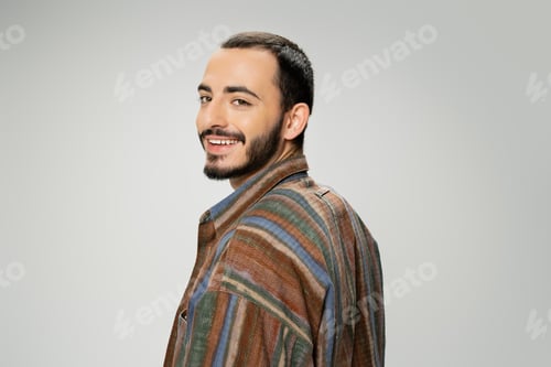 Preview: portrait of joyful bearded man in trendy shirt looking at camera isolated on grey
