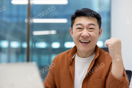 Preview: Asian man businessman celebrating success at work, smiling confidently in modern office environment
