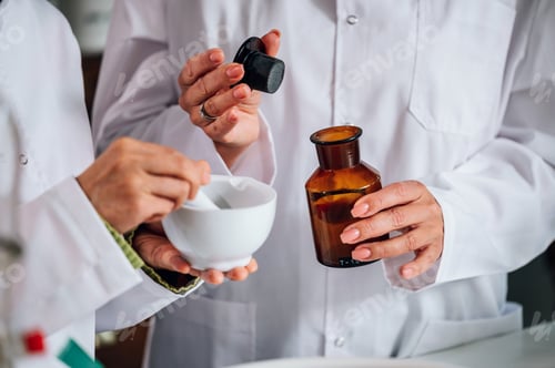 Preview: Close-up of the pharmacists' hands mixing medicine in a mortar and adding liquid to it.