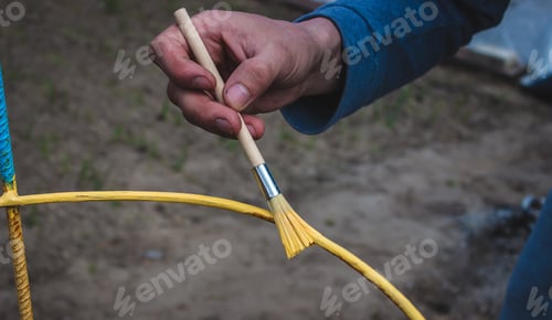 Preview: a man paints an iron frame with yellow and blue paint.