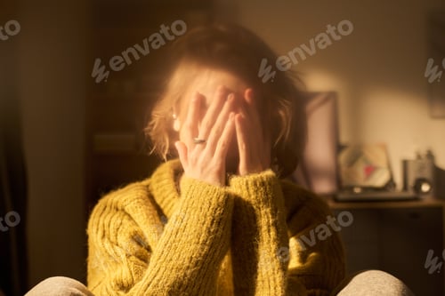 Preview: Young Woman Covering Face with Hands Sitting Indoors