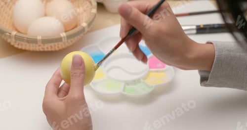 Preview: Coloring eggs for Easter with hands and a brush with watercolor paints