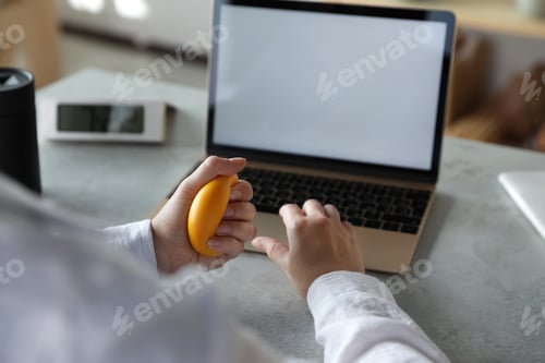 Preview: Woman squeezing antistress ball while working on laptop in office, closeup