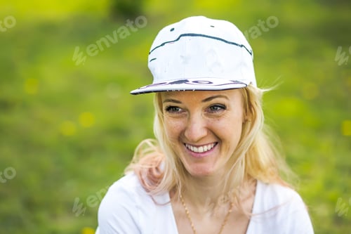Preview: Happy woman in white baseball cap on green grass background