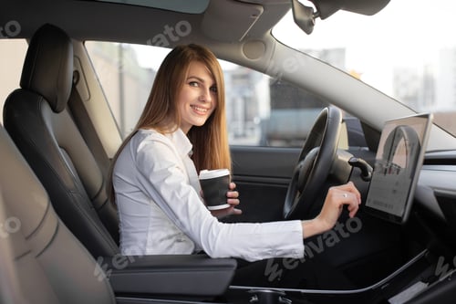 Preview: Businesswoman drinks coffee to go, sits behind wheel in modern luxury electric car