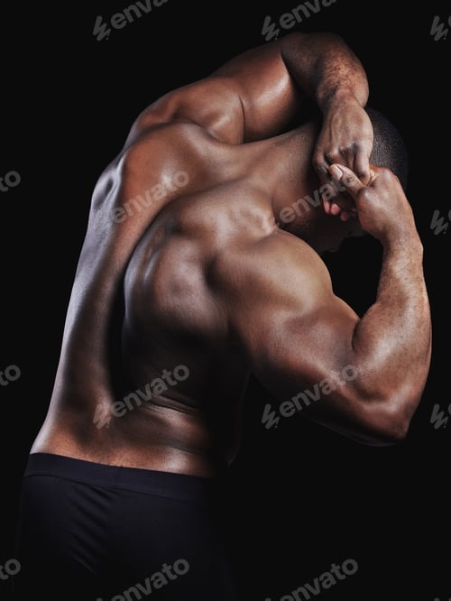 Preview: Rearview studio shot of a fit young man flexing against a black background