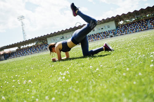 Preview: Portrait of a beautiful woman in sportswear stretching her muscles in the stadium.