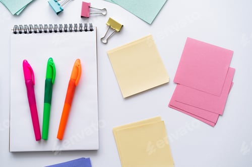 Preview: top view of colorful pens on notebook near blank paper notes and fold back clips on white