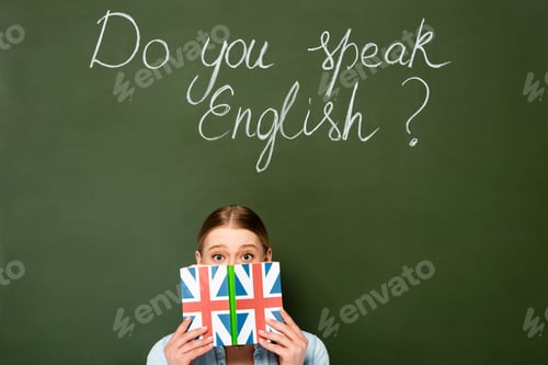 Preview: pretty girl with obscure face holding book with uk flag near chalkboard with do you speak English