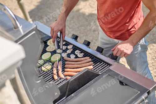 Preview: A man in red shirt standing near the barbecue grill and cooking veggies