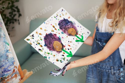 Preview: Girl child holds and shows drawing on paper drawn with hands and fingers with acrylic paints