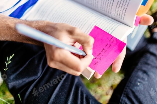 Preview: Midsection of student writing on adhesive note in book at park