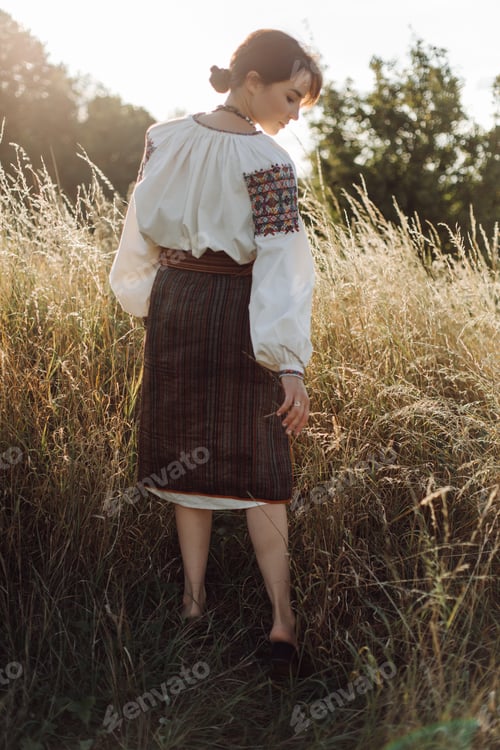 Preview: Young woman in traditional national embroidered shirt and skirt on nature at sunset.