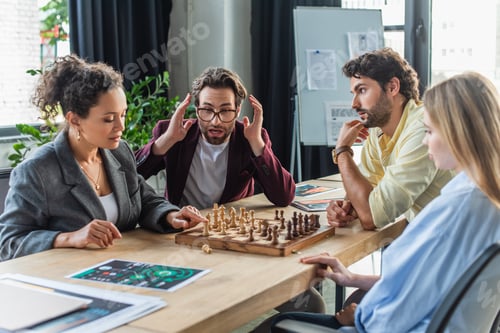 Preview: Shocked businessman sitting near multiethnic colleagues playing chess in office