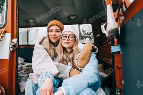 Preview: Portrait of two cheerful young women friends sitting in a van in winter camp.