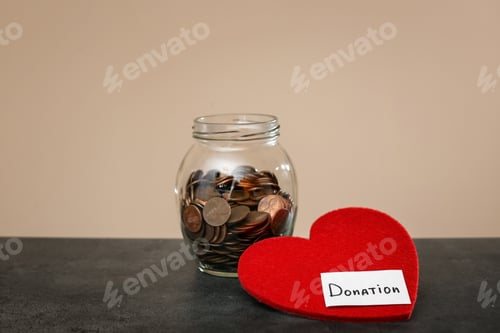 Preview: Donation jar with coins and red heart on table against color background