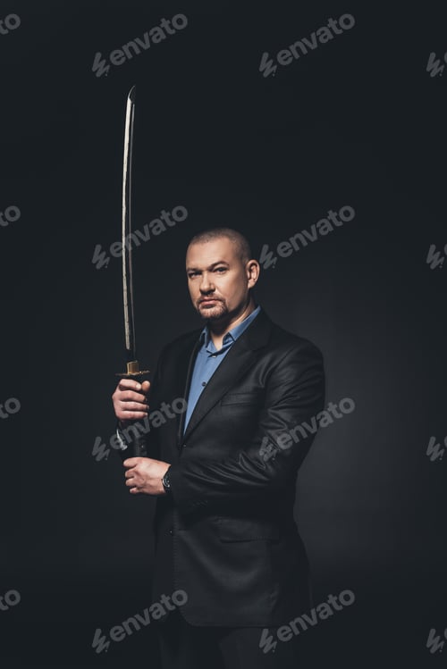 Preview: modern samurai in formal suit with katana sword looking at camera on black