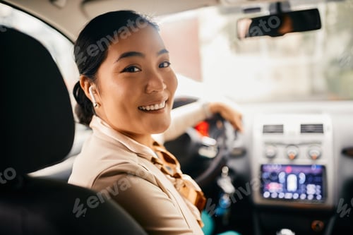 Preview: Happy Asian businesswoman driving a car in reverse and looking at camera.