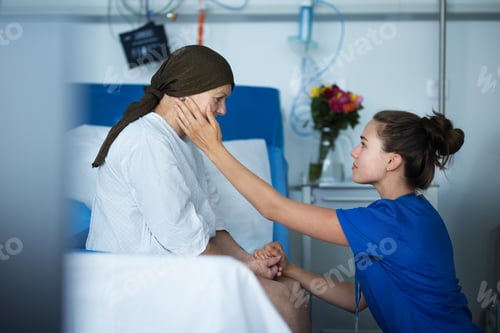 Preview: Empathic nurse taking care of senior woman with cancer, stroking her cheek.