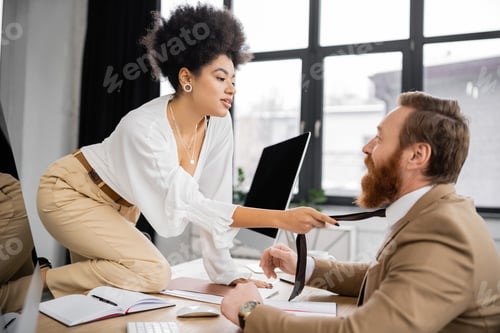 Preview: african american businesswoman pulling tie while seducing bearded coworker in office