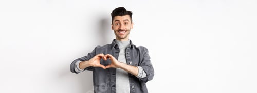 Preview: Smiling boyfriend showing heart with love, looking romantic and happy at lover, standing on white
