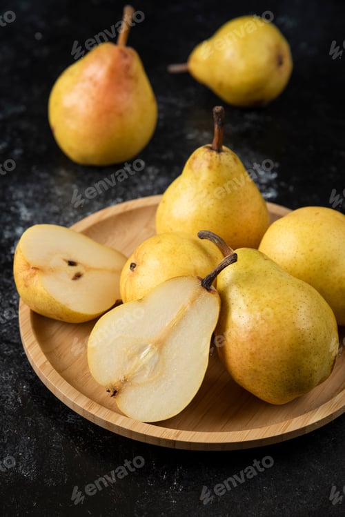 Preview: Wooden plate of delicious yellow pears on black surface
