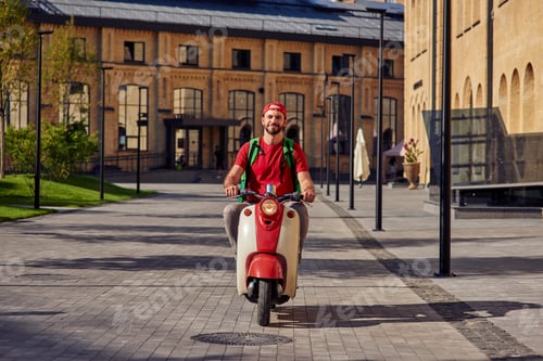 Preview: Young cheerful caucasian male courier with thermo bag delivering food to customers, riding scooter
