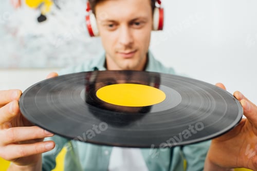 Preview: Selective focus of young man in headphones holding vinyl record at home